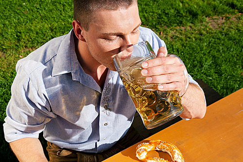 Man in traditional Bavarian costume - Lederhosen - drinking beer and eating pretzel