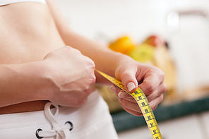 Thin and beautiful woman (only torso) measuring her waist with a tape measure|in the background fruit in a bowl