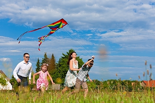 Happy family - mother|father|children - running over a green meadow in summer; they are flying a kite