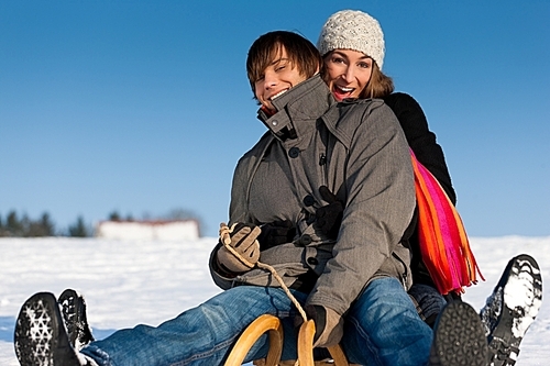 Happy couple in winter sitting on sled in the snow