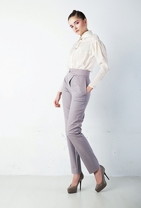 Young pretty brunette woman in white shirt and blue trousers in studio. Fashion style