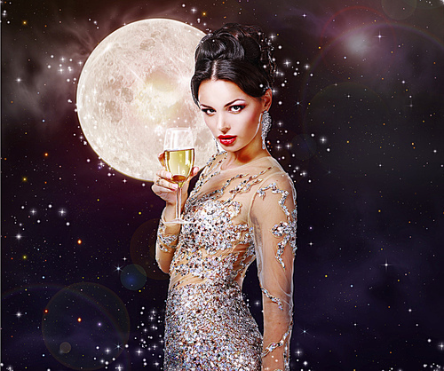Romantic girl in the beautiful dress with a glass of champagne against the night sky with magical stars and moon.