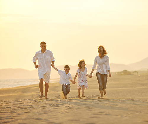 happy young family have fun on beach run and jump  at sunset