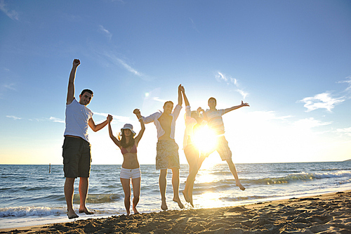 happy young friends group have fun and celebrate while jumping and running on the beach at the