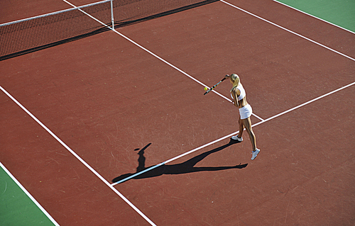 young fit woman play tennis outdoor on orange tennis field at early morning