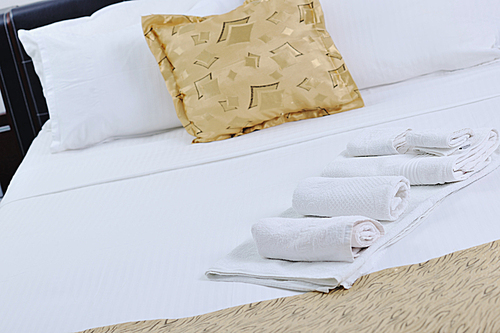 white towels on bed in luxury hotel room with yellow pillow in background