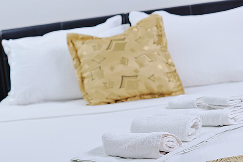 white towels on bed in luxury hotel room with yellow pillow in background