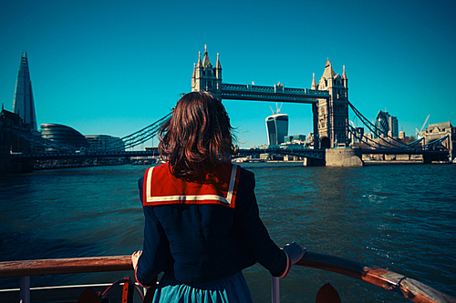 A young woman on a boat is looking at Tower bridge and the London skyline