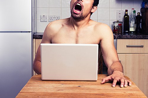 Young man is watching pornography on his laptop in the kitchen