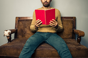 Young man is sitting on a sofa and reading