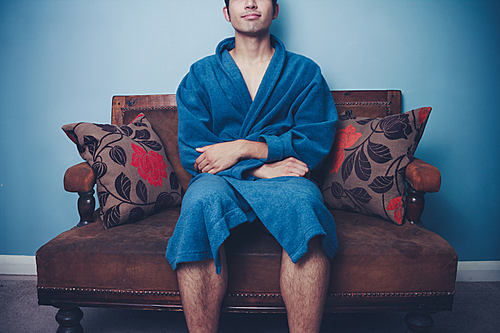 Young man in bathrobe sitting on sofa