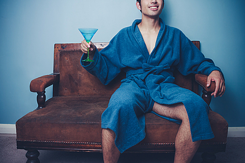 Man in bathrobe sittin on sofa with cocktail glass