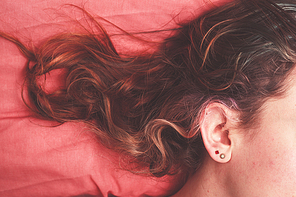 Young woman lying in bed with her hair strewn across the pillow