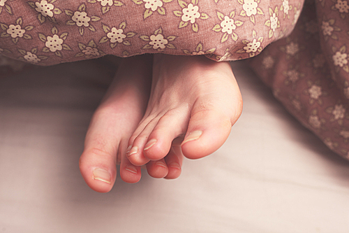 Young woman’s feet in bed under the covers