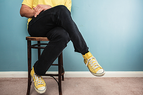 Below the neck shot of a young man sitting on a chair against a blue wall