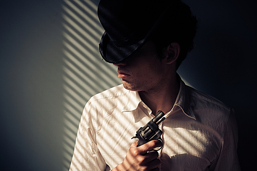 Young man with gun by the window is covered in shadows from the blinds