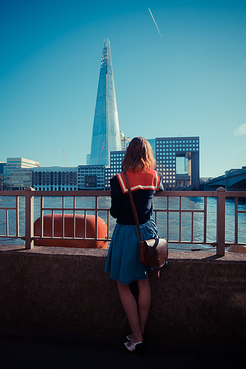 A young woman is standing by the Thames and looking at the Shard