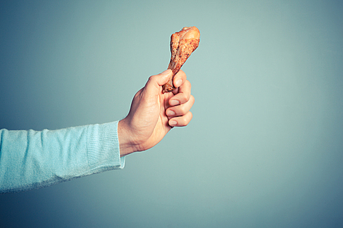 A young man is holding a roasted chicken drumstick