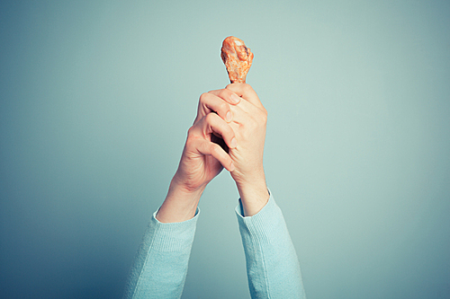 A young man is holding a roasted chicken drumstick