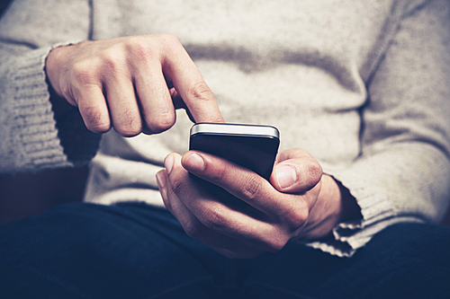 Closeup on a man’s hands as he is sitting on a sofa and using a smartphone