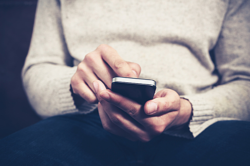 Closeup on a man’s hands as he is sitting on a sofa and using a smartphone