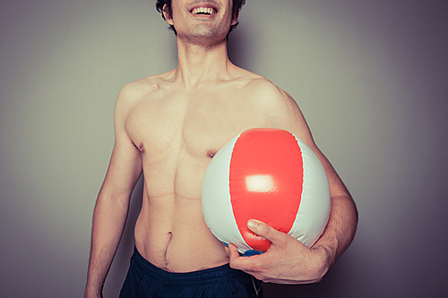 An athletic young man is holding a beach ball