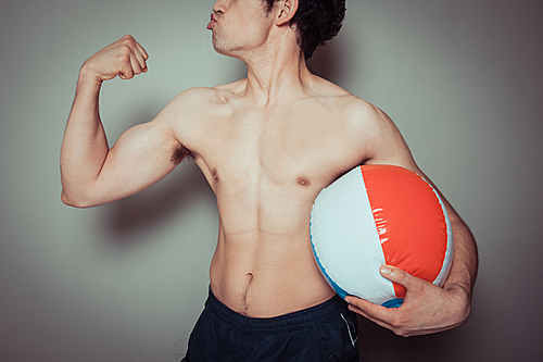 An athletic young man is holding a beach ball