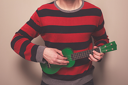 Young man in a striped jumper is playing ukulele