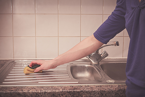 A young woman is cleaning around the kitchen sink