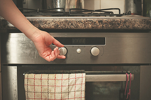 The hand of a young woman is turning the knob on a stove