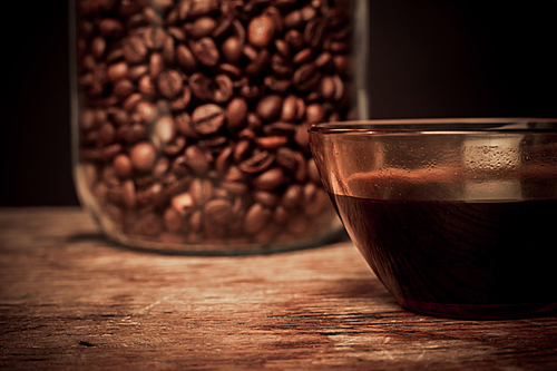 Cup of black coffee and jar of beans on a wooden table