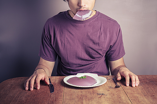 A young man is sitting at a table and eating a purple jelly pudding