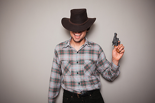 A young man wearing acowboy hat and a plaid shirt is holding a revolver