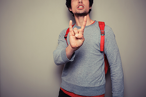 Young man wearing a red backpack is diplaying a heavy metal gesture