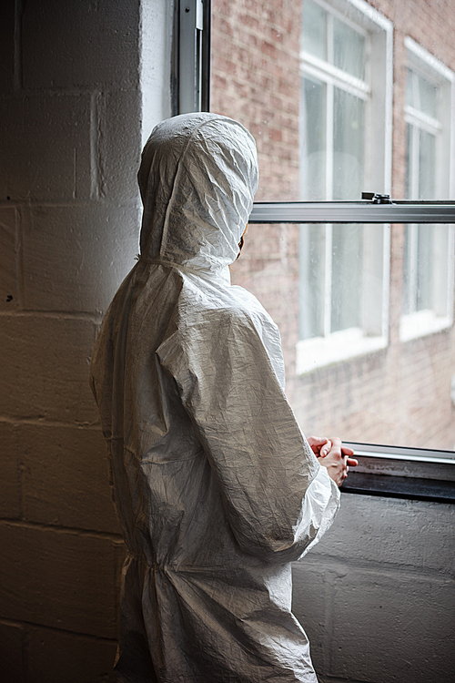 A scientist wearing a boiler suit is standing by  a window