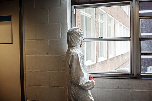 A scientist wearing a boiler suit is standing by  a window