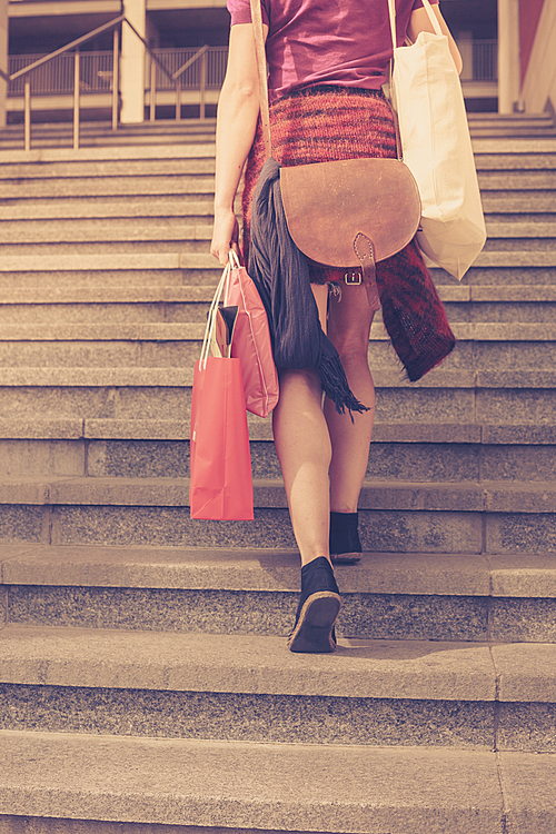 A young woman with shopping bags is walking up the stairs outside at sunset