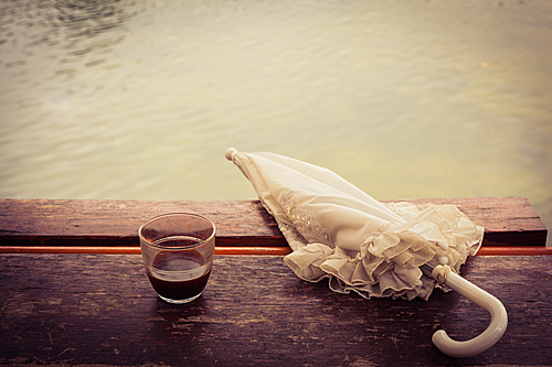 A cup of coffee and an umbrella on a wooden table by a lake in the afternoon