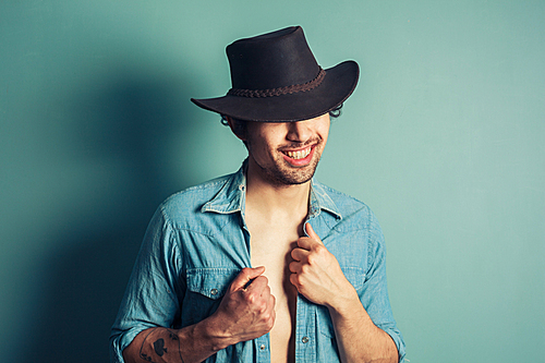 a  young cowboy is standing by a blue wall with his shirt unbuttoned