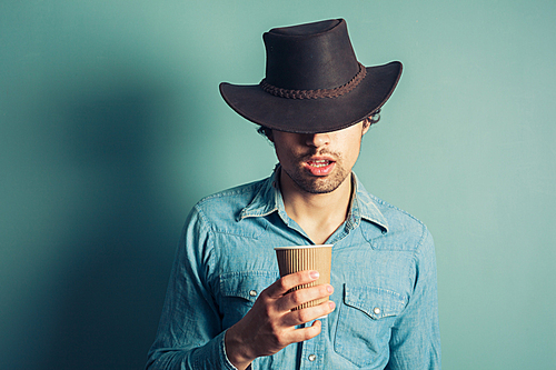 Young cowboy is drinking coffee from a paper cup