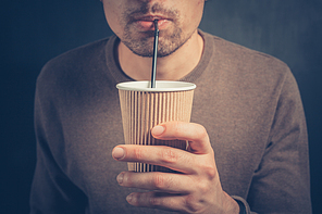 A young man is using a straw to drink from a paper cup