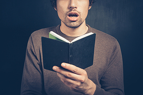 A surprised young man is holding a small notebook