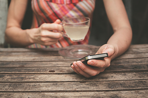 A young woman is drinking tea and using her smart phone at a wooden table