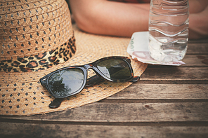 A hat and a pair of sunglasses on a table outside with a woman in the background