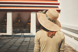 A young woman wearing a hat is exploring a buddhist temple