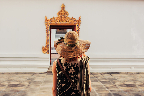 A young woman is looking at the elaborate entrance to a buddhist temple