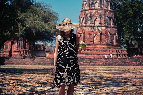 A young woman is drinking juice from a coconut near the ruins of an ancient buddhist temple