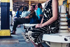 A young woman is seated and is waiting on the platform in a train station