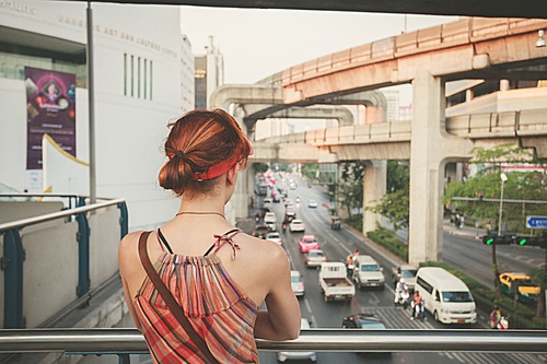 A young woman is looking at the traffic from an overpass in Bangkok