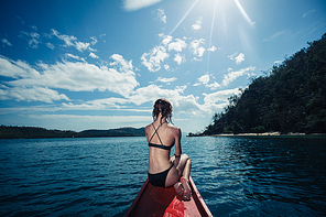 a  young woman wearing a bikini is sitting on a small boat near a tropical island